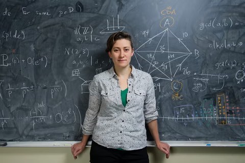 Moon Duchin standing in front of a chalkboard covered in mathematical notation